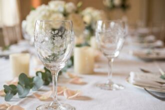 Deux verres en cristal gravés avec des initiales et des motifs floraux délicats, posés sur une nappe blanche lors d'une réception de mariage élégante