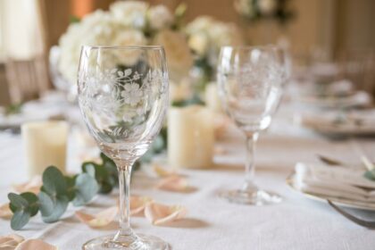 Deux verres en cristal gravés avec des initiales et des motifs floraux délicats, posés sur une nappe blanche lors d'une réception de mariage élégante